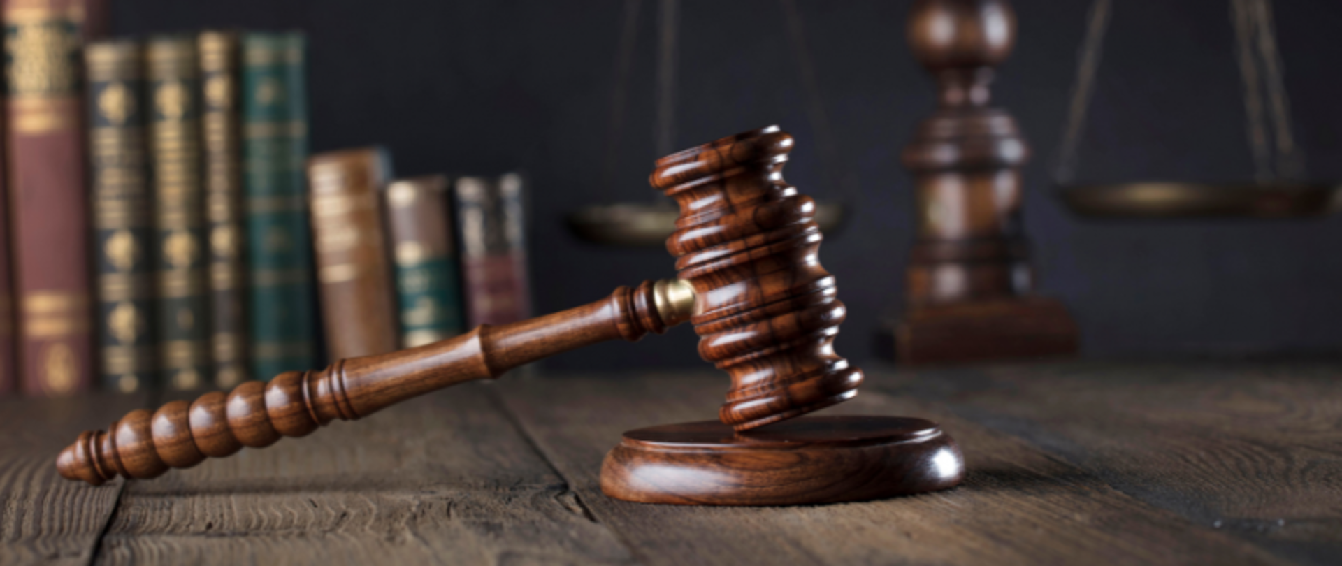 Blat biurka. Na nim młotek sędziowski na podstawce. W tle książki.