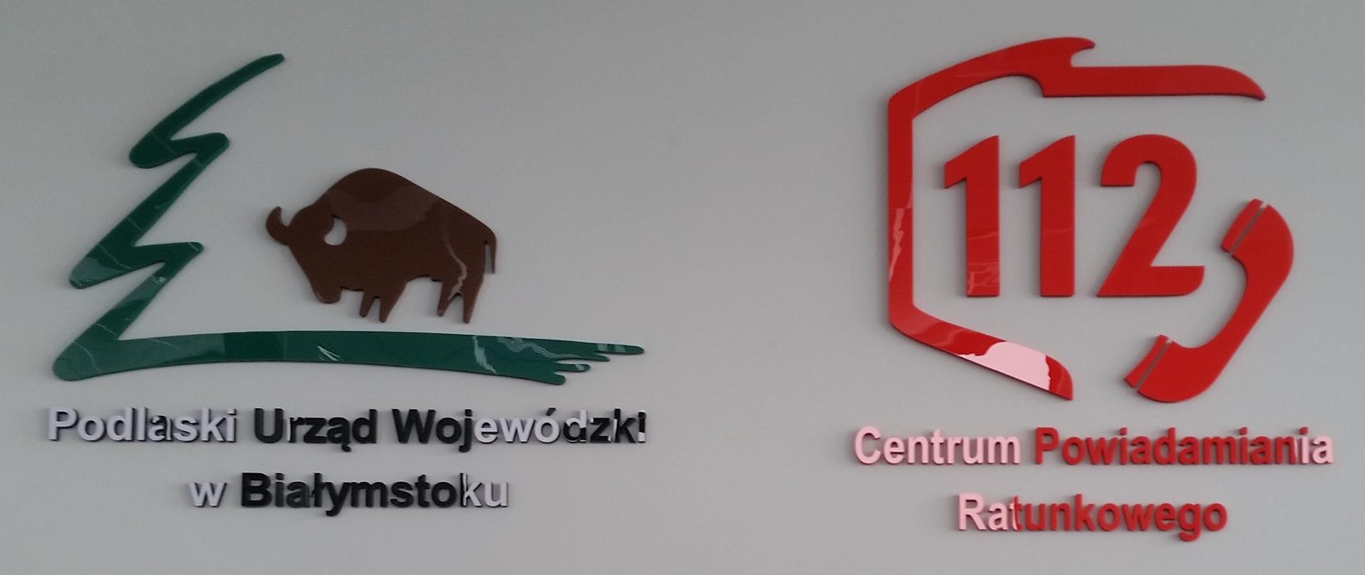 Umieszczone na ścianie logotypy Podlaskiego Urzędu Wojewódzkiego oraz Centrum Powiadamiania Ratunkowego.