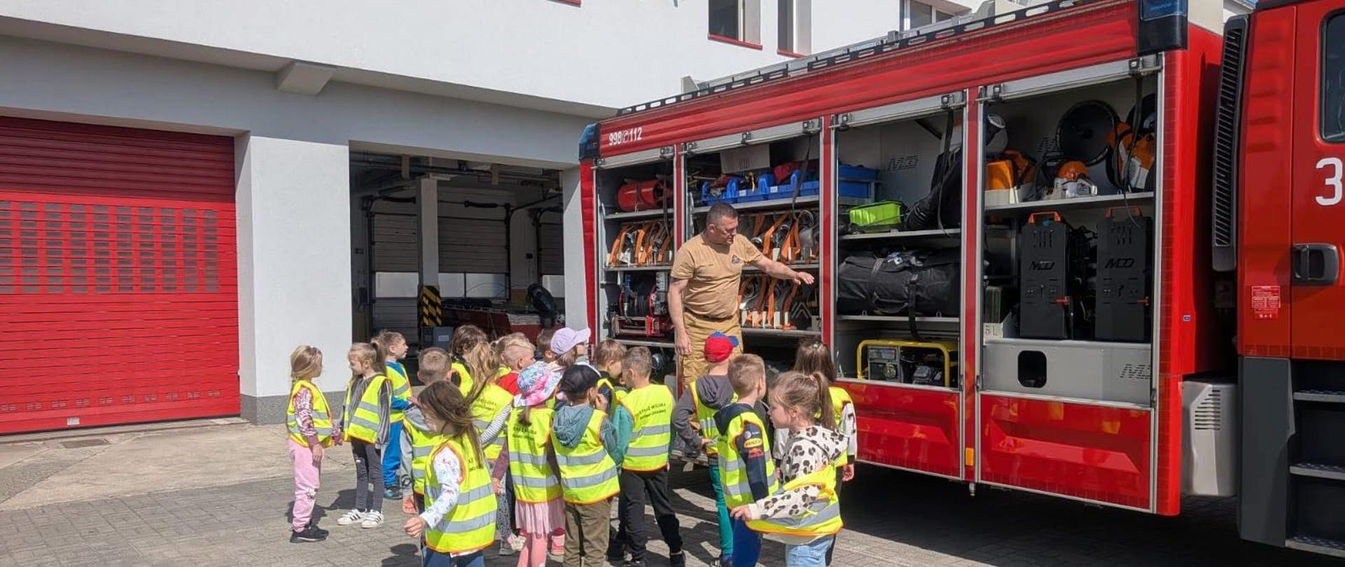 Na zdjęciu strażak prezentuje dzieciom sprzęt ratowniczo-gaśniczy podczas pokazu edukacyjnego.