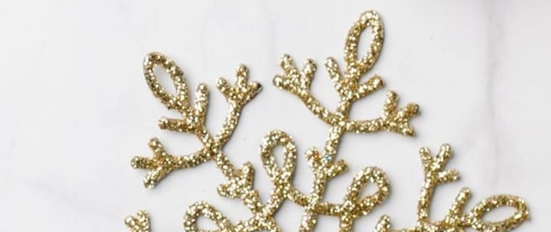 Na białym tle, po lewej stronie, umieszczone zostały życzenia świąteczne. Poniżej znajduje się podpis dyrektora szkoły wraz z datą. w tle widoczne są grafiki świąteczne - złote bombki, ozdoby choinkowe oraz zielone gałązki. W górnej części umieszczone zostało logo szkoły.