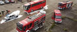 Zdjęcie przedstawia ćwiczenia straży pożarnej. Widać na nim autokar oraz wozy strażackie oraz rozbite auto.
