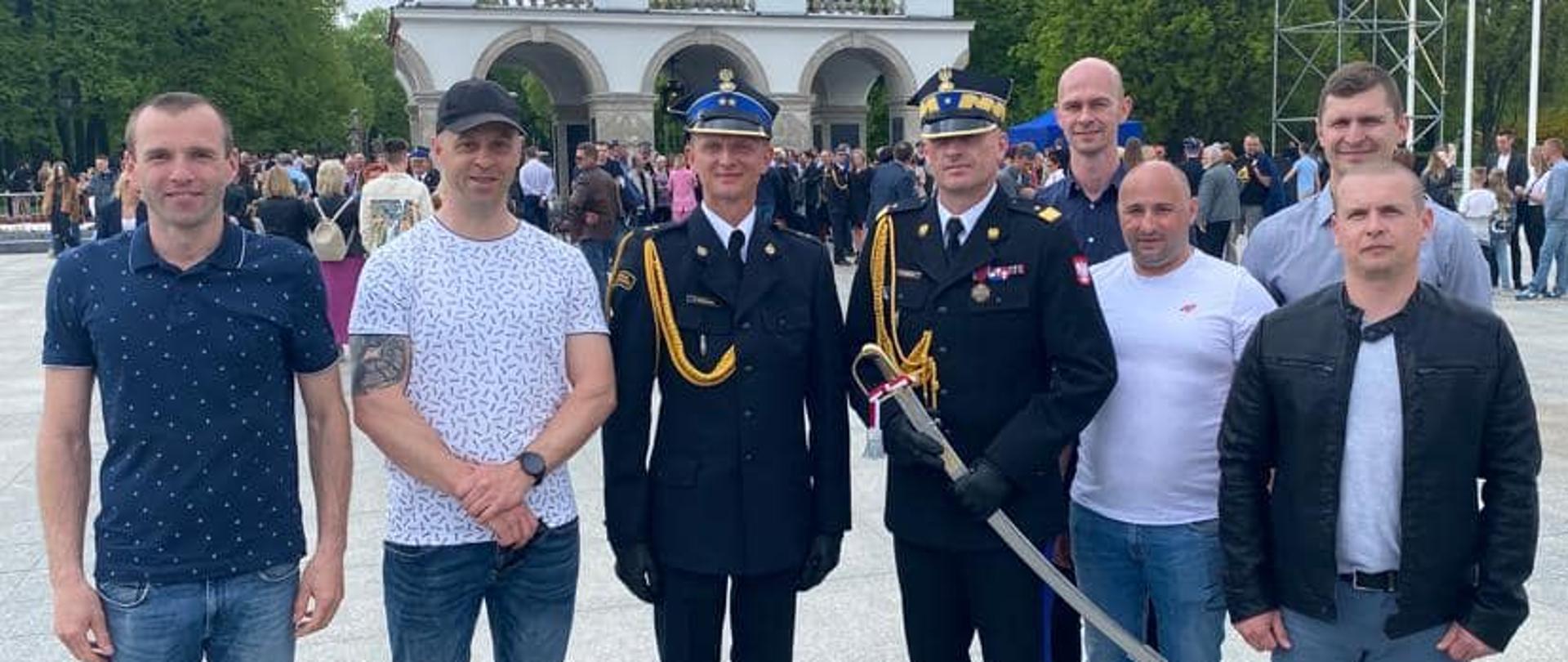 Zdjęcie przedstawia strażaka podczas awansu na pierwszy stopień oficerski podczas Centralnych Obchodów Dnia Strażaka w Warszawie stojący z Zachodniopomorskim Komendantem Wojewódzkim PSP, przyjaciółmi oraz rodziną.