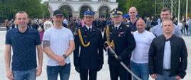 Zdjęcie przedstawia strażaka podczas awansu na pierwszy stopień oficerski podczas Centralnych Obchodów Dnia Strażaka w Warszawie stojący z Zachodniopomorskim Komendantem Wojewódzkim PSP, przyjaciółmi oraz rodziną.