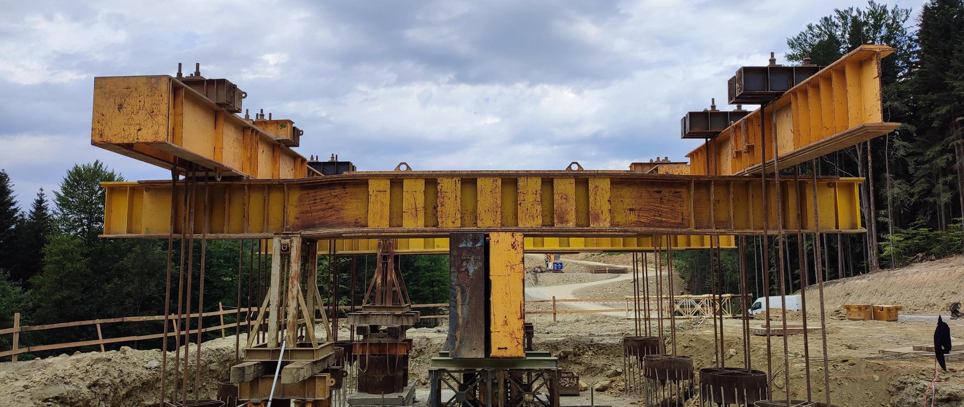 Widok z poziomu ziemi na budowę estakady i specjalną konstrukcję stalową do próbnego obciążenia. Sprawdzenie nośności wykonano metodą belki odwróconej. Na pierwszym planie widać mierniki stojące na statywach.