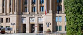 Widok na wejście do budynku Ministerstwa Finansów. Przed gmachem znajdują się maszty z flagami oraz podjazd z poręczami.