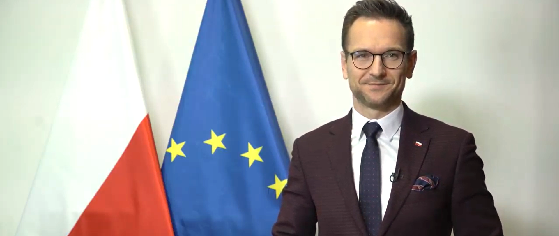 wiceminister Waldemar Buda, za nim stoją flagi Polski i Unii Europejskiej