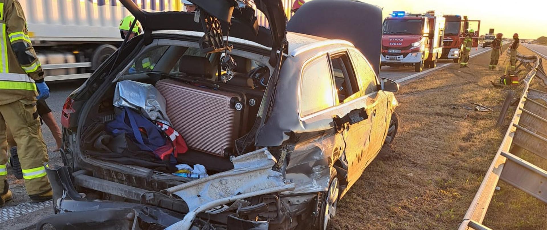 Uszkodzony samochód stoi na pasie zieleni przed nim samochody strażackie