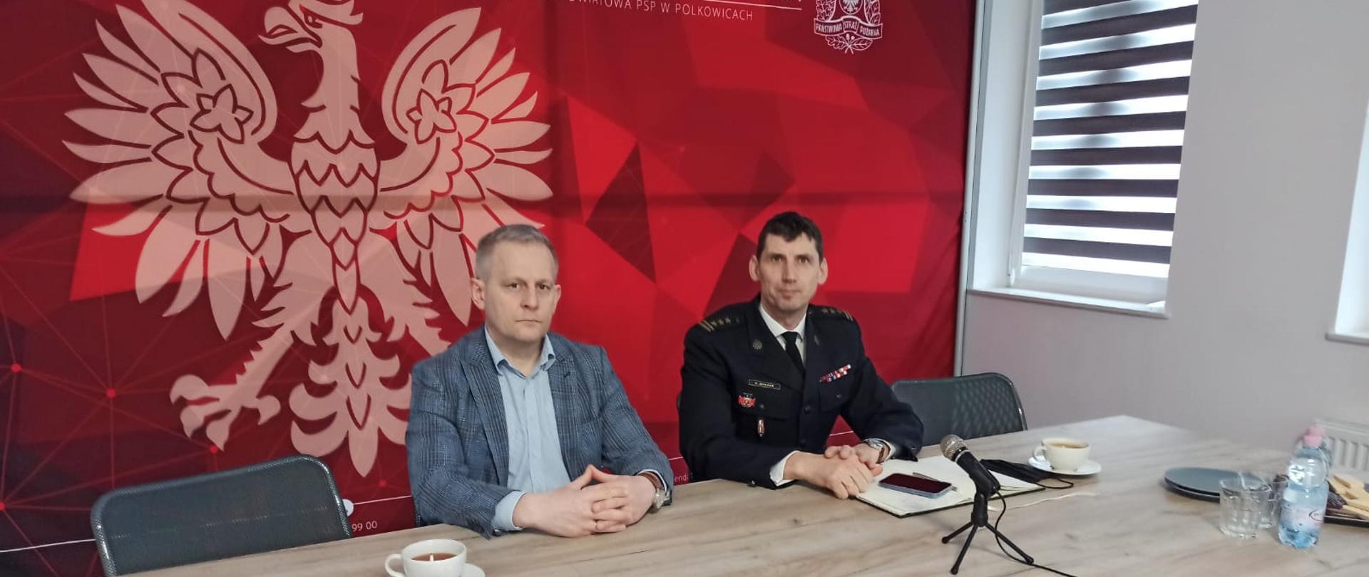 Zdjęcie Starosty Polkowickiego Kamila Ciupak oraz Komendanta Powiatowego PSP w Polkowicach st. bryg. Sylwestera Jatczaka na tle grafiki logotypowej PSP