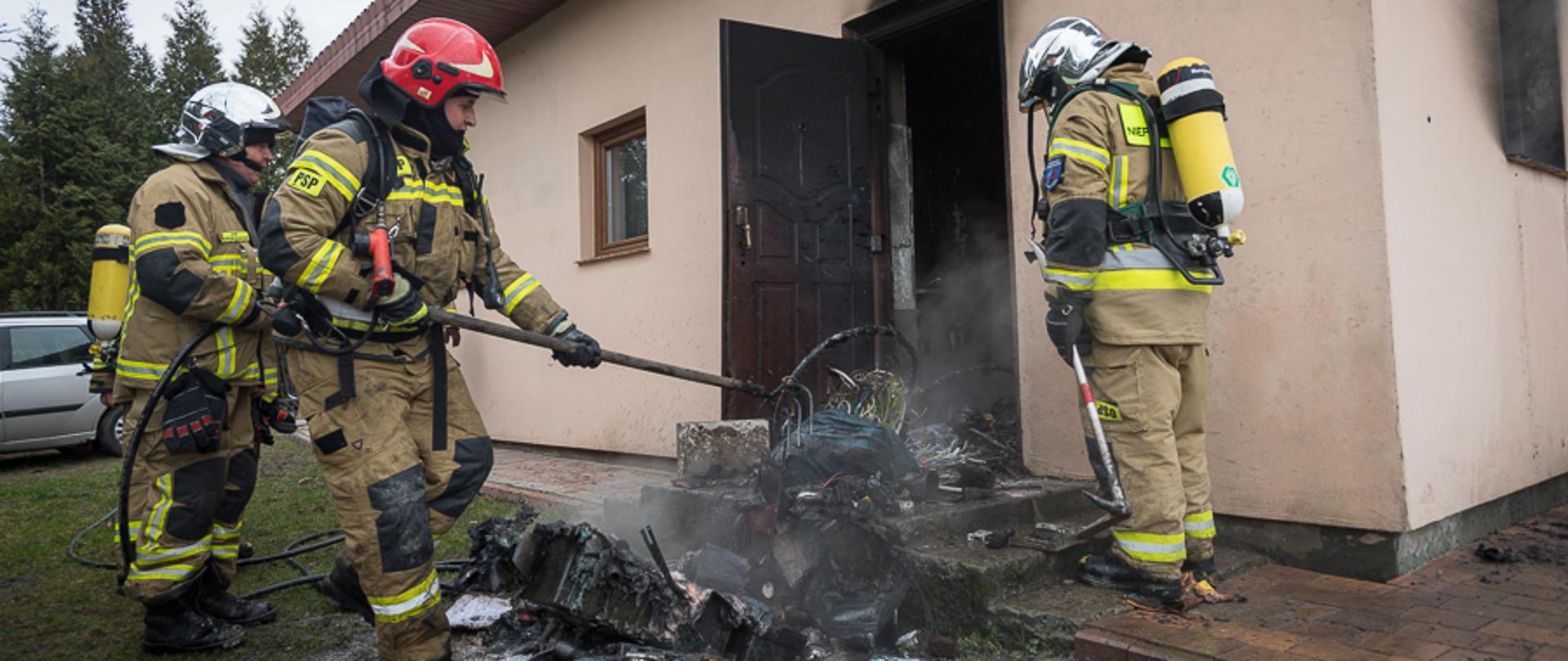 Trzech strażaków wyciąga z wnętrza kotłowni spalone wyposażenie.