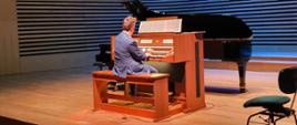 Mężczyzna gra na organach siedząc tyłem do publiczności na scenie sali koncertowej PSM.