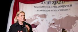 Minister Barbara Nowacka przemawia z mikrofonem na scenie na tle mapy świata i napisu XVIII Zjazd Nauczycieli Polonijnych i Komitetów Rodzicielskich 