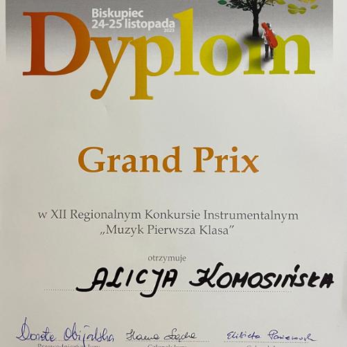 Na zdjęciu widać dyplom z nagrodą Grand Prix XII Regionalnego Konkursu Instrumentalnego "Muzyk pierwsza klasa". Dyplom jest utrzymany w tonacji koloru białego. 