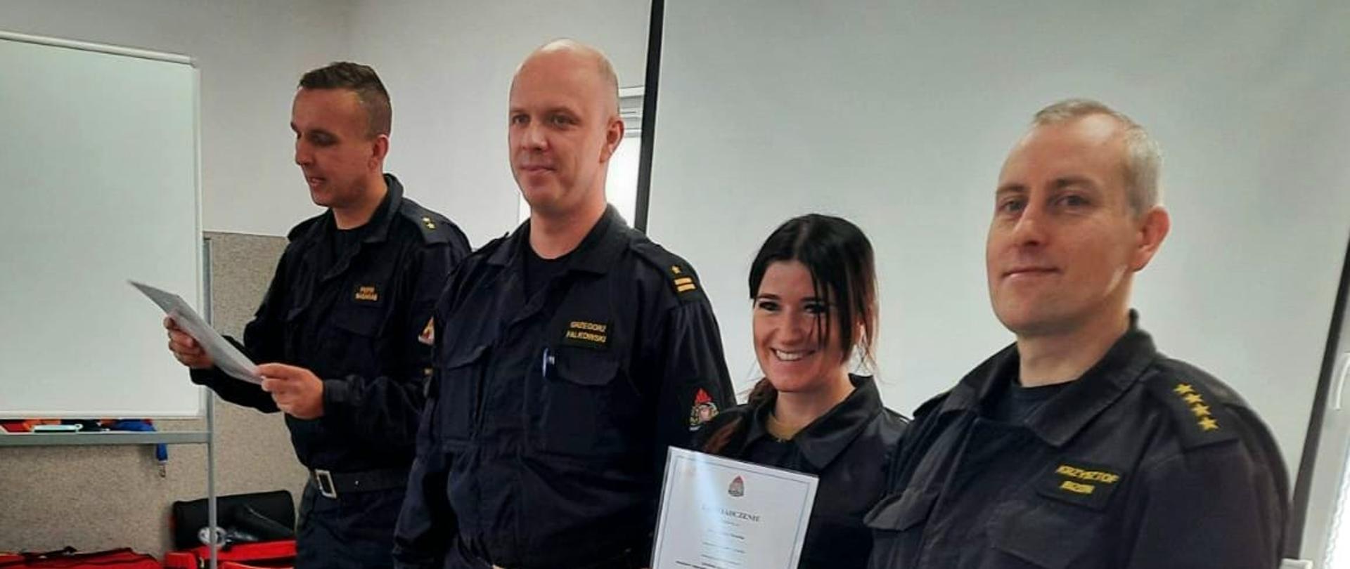Zdjęcie przedstawia mł. bryg. Grzegorza Falkowskiego, Zastępcy Komendanta Miejskiego PSP w Słupsku, st. kpt. Krzysztofa Bizona, Dowódcy JRG nr 2 w Słupsku oraz mł. kpt. Piotra Basaraba, Naczelnika Wydziału Operacyjno-Szkoleniowego KM PSP w Słupsku oraz uczestniczkę kursu