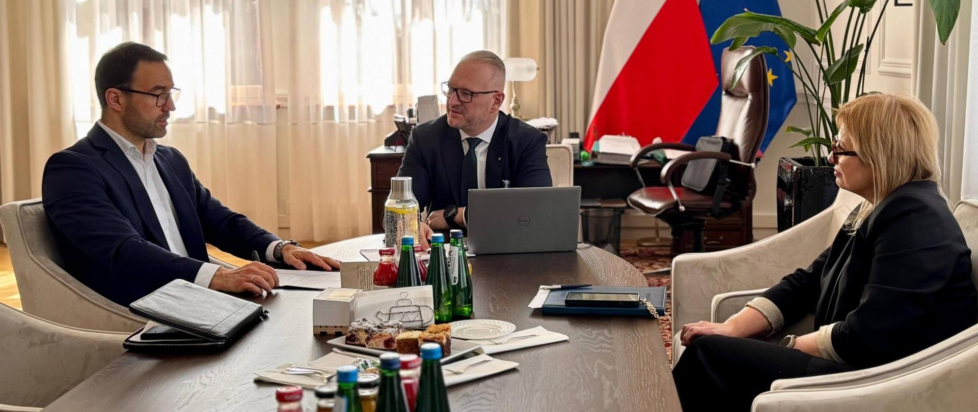 Grupa oficjeli, w tym wojewoda, siedzi przy stole, rozmawiają 