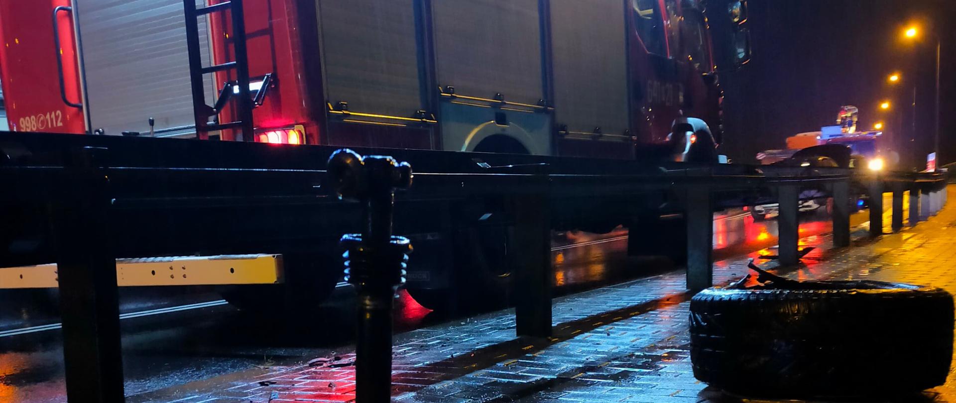 Noc. Zdjęcie przedstawia rozbite części auta osobowego. W tle auto strażackie.