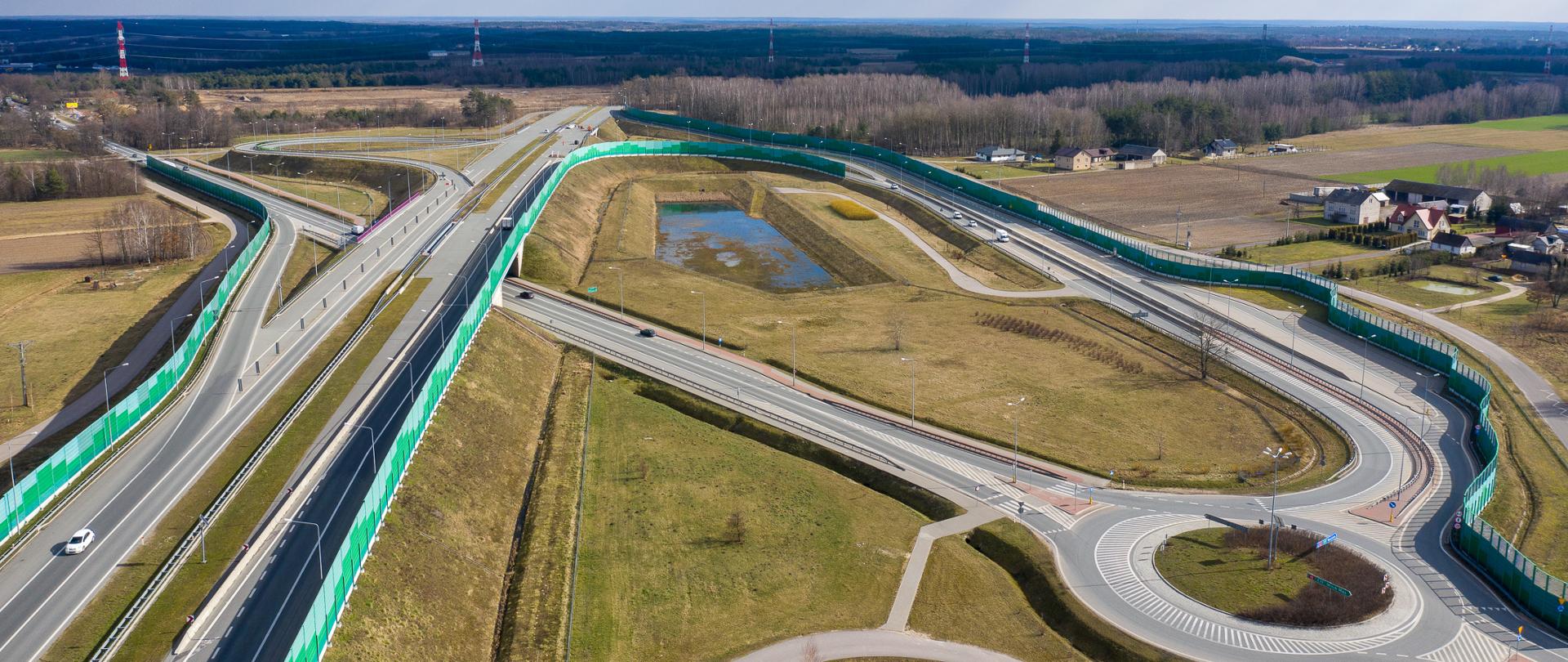 Widok z powietrza na węzeł Kałuszyn na A2 gdzie obecnie kończy się autostrada A2. Po lewej dwujezdniowa autostrada przechodząca wiaduktem nad drogą krajową nr 2 i łącznice węzła z rondem na połączeniu z DK2. Na horyzoncie widać drzewa. 