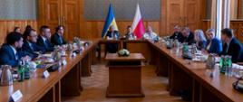 Szerokie ujęcie sali konferencyjnej. Przy długim stole po prawej stronie siedzą m.in. Barbara Nowacka i Radosław Sikorski. Minister Nowacka gestykuluje podczas rozmowy z siedzącymi naprzeciwko przedstawicielami Ukrainy. W tle, na środku ściany, widoczne są flagi Ukrainy i Polski.