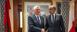 Na zdjęciu podający sobie ręce minister Tomasz Siemoniak (po lewej) i dyrektor Hammouchi (po prawej). Po prawej stoi biało-czerwona flaga Polski, a po lewej czerwono-zielona flaga Maroka. Za flagami widać kolumny z kolorowymi wzorami. Za ministrami zdjęcie mężczyzny w złotej ramie.