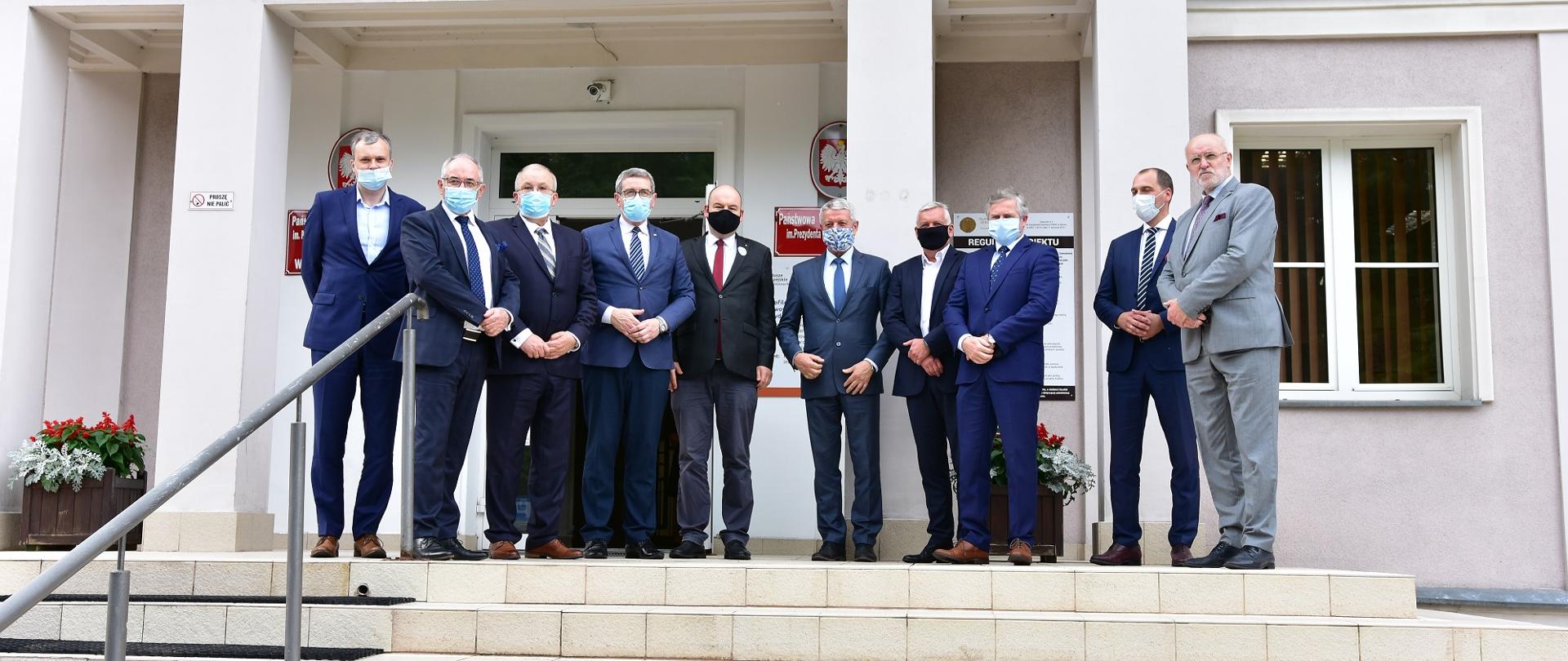 Uczestnicy spotkania stoją na schodach przed wejściem do uczelni.