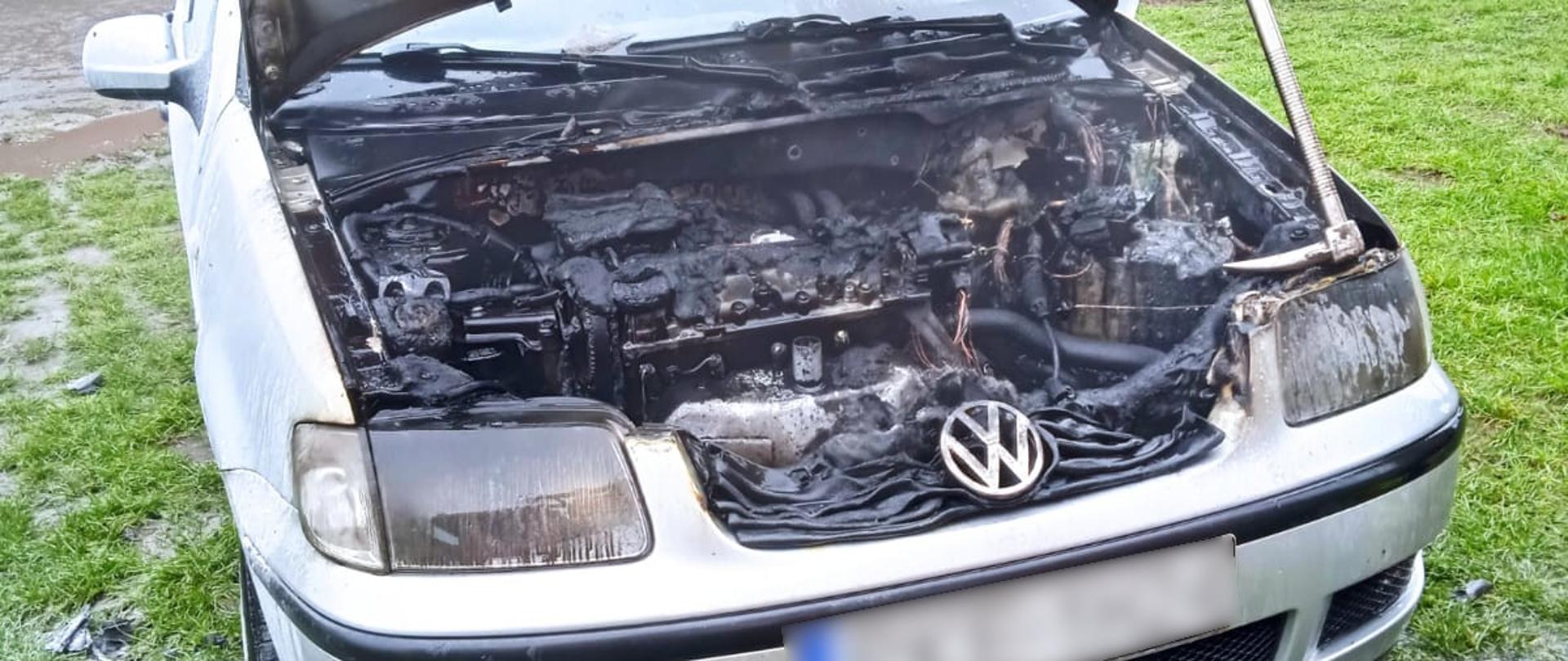 Miejsce zdarzenia widoczny szary samochód osobowy z uniesiona pokrywa silnika oraz spaloną komora silnika