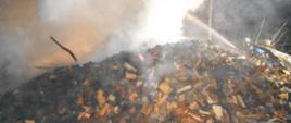 Zdjęcie przedstawia strażaków gaszących pożar sterty porąbanego drewna