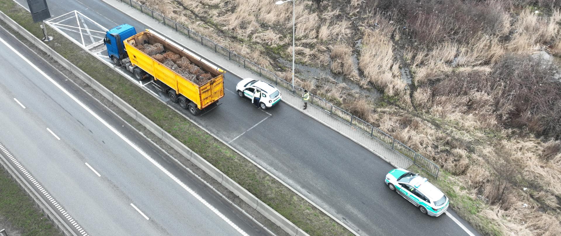 Widok z góry na pojazd ciężarowy transportujący odpady z obróbki metali, po prawej stronie dwa oznakowane pojazdy: Inspekcji Ochrony Środowisko oraz Straży Granicznej;
