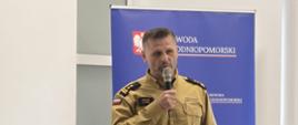 Funkcjonariusz Państwowej Straży Pożarnej przemawia do uczestników spotkania. W tle widoczny baner Wojewody Zachodniopomorskiego.