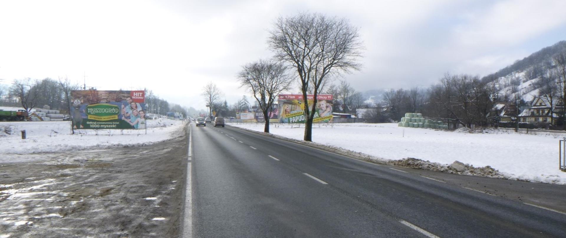 droga w zimie, prosty odcinek, pogoda pochmurna, w tle widoczne zabudowania
