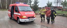 Na zdjęciu samochód pożarniczy, oraz osoba przewożona na szczepienie w asyście strażaków. 