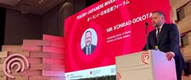 Wiceminister Konrad Gołota stoi za mównicą. W tle ekran z napisem: Polish-Japanese Investment Forum.