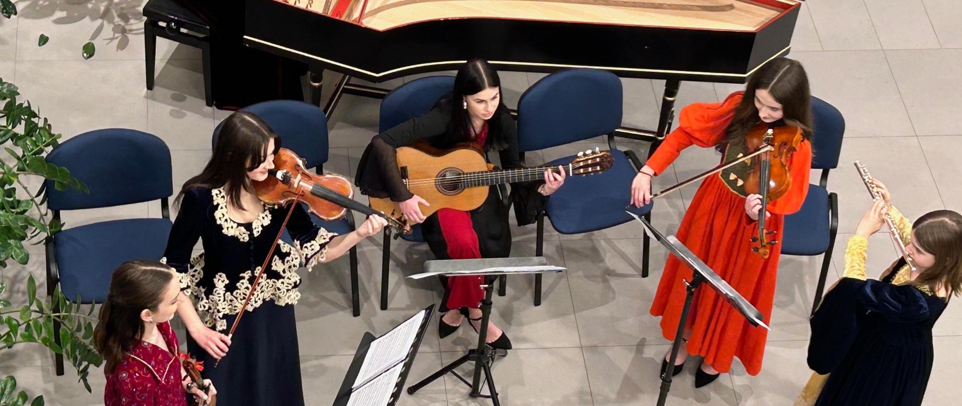 Muzycy zespołu Melodiam Flores grają na skrzypcach, flecie, gitarze i klawesynie podczas wydarzenia artystycznego w sali wystawowej.