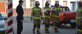 Dzień Flagi Rzeczypospolitej Polskiej. Plac przed Komendą Powiatową PSP w Rawiczu. Na nim strażacy z jednostki ratowniczo-gaśniczej w ubraniach specjalnych podczas okolicznościowej zbiórki. Na pierwszym planie poczet flagowy maszerujący w stronę masztu. W tle samochód rozpoznawczo-ratowniczy. Obok masztu stoi zastępca dowódcy JRG w ubraniu dowódczo-sztabowym.