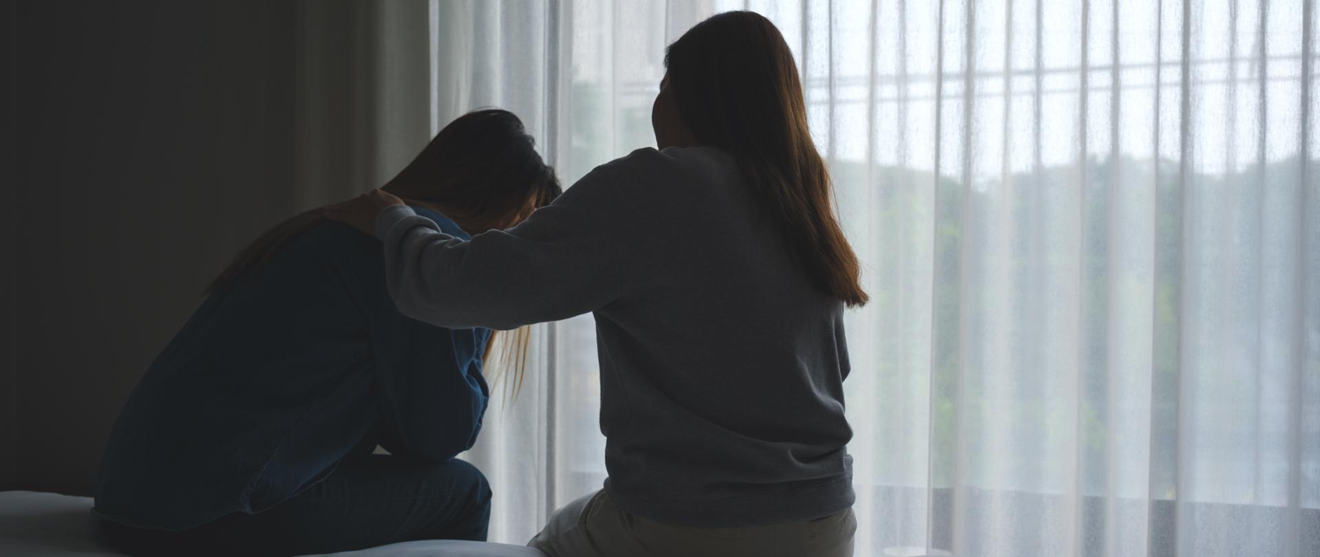 Silhouette image of a woman touching her friend shoulder to comforting and giving encouragement in bedroom