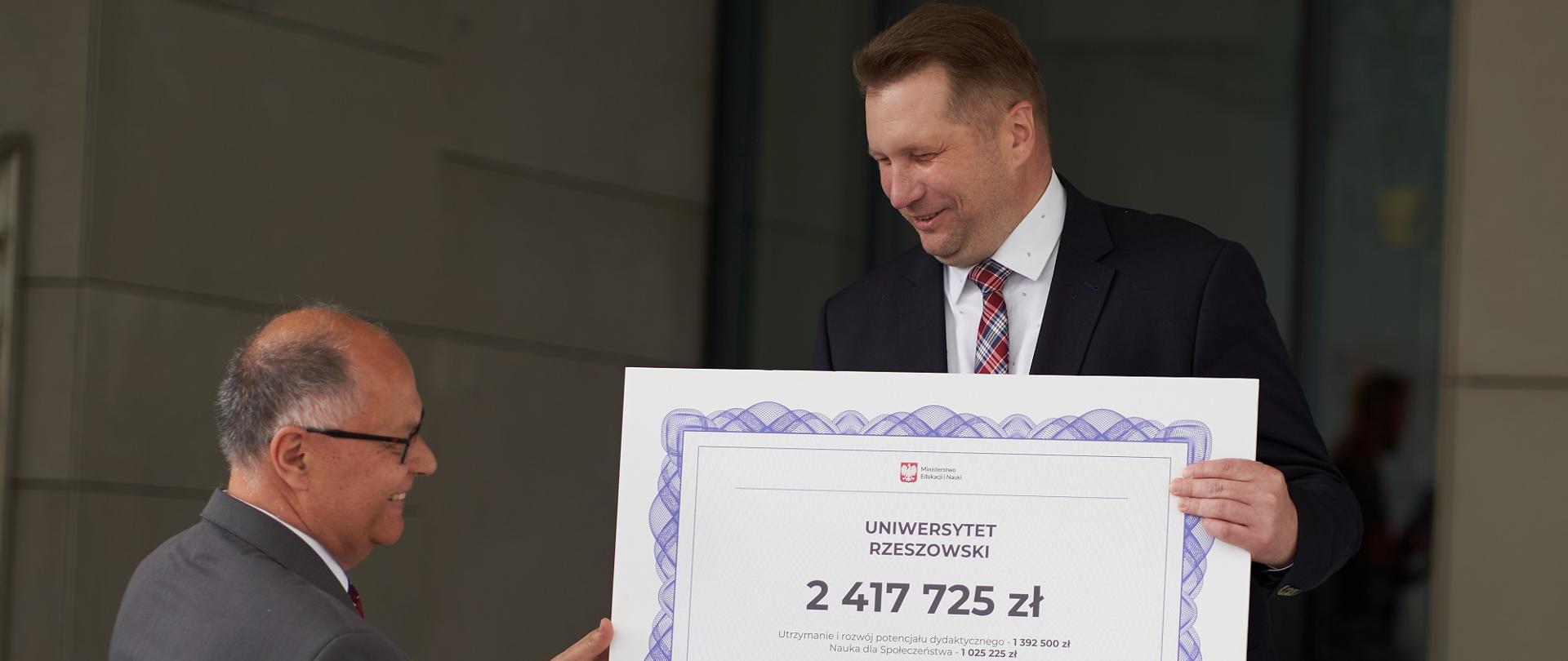 Minister pokazuje wielki symboliczny czek na kwotę 2 417 725 zł.