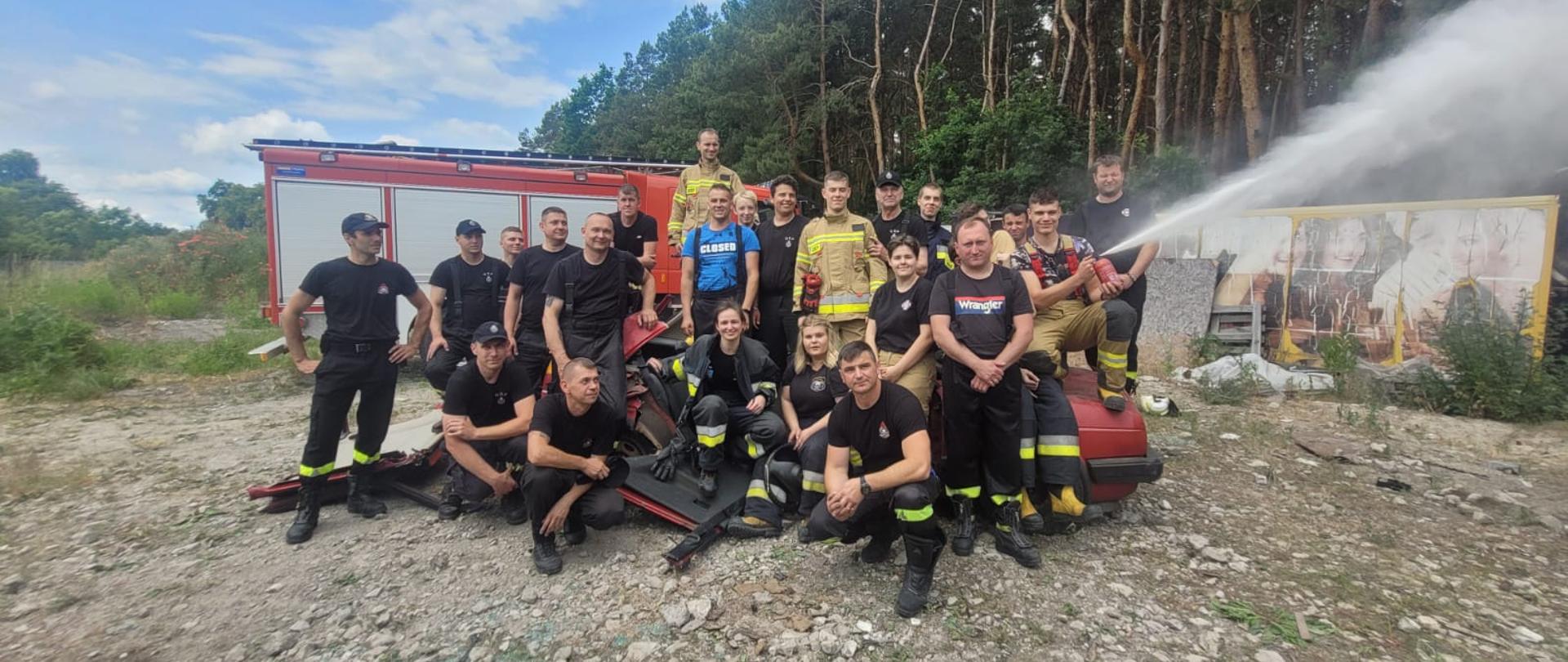 strażacy w grupie podczas szkolenia podstawowego dla OSP, w tle samochód pożarniczy