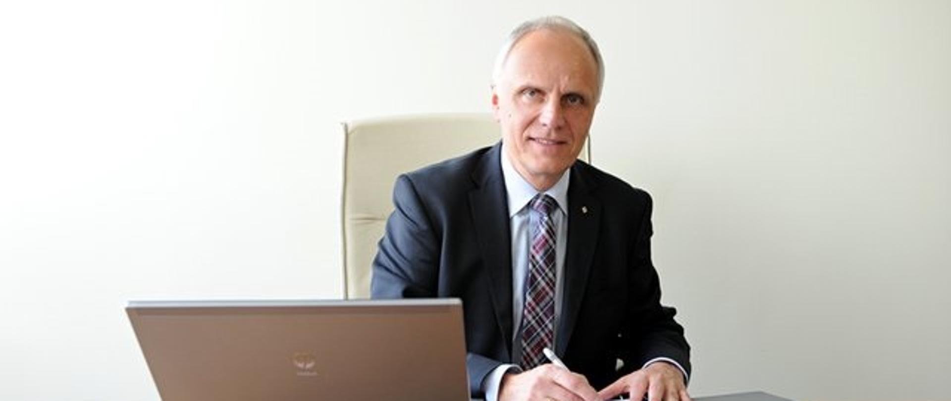 Mężczyzna w garniturze siędzący przy biurku podczas podpisywania dokumentów.