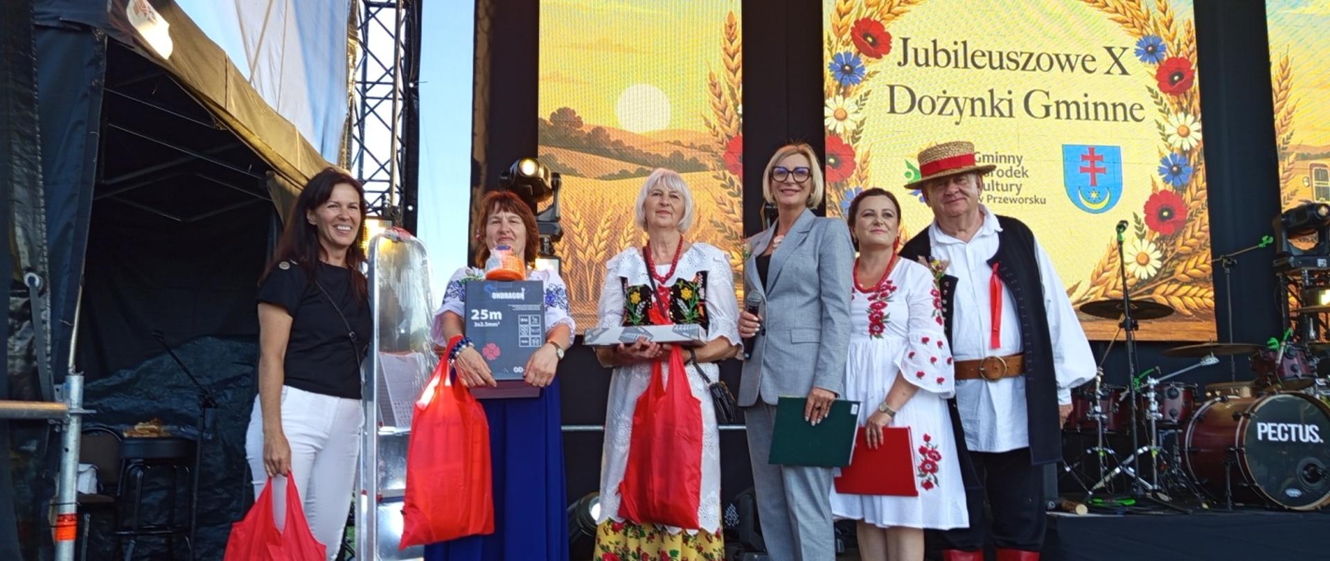 Osoby stoją na scenie. Laureaci trzymają w rękach wygrane nagrody. 