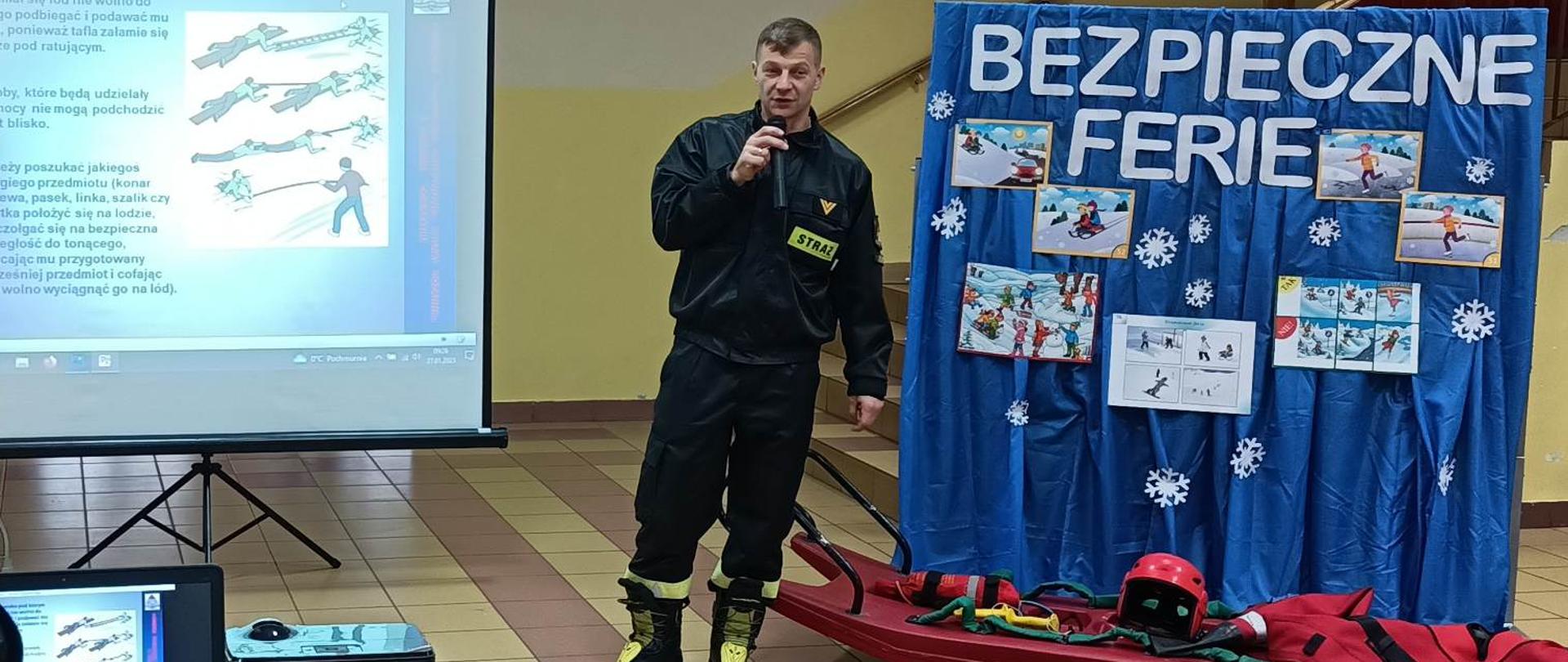 Dwóch strażaków w ramach akcji Bezpieczne Ferie na rzutniku przedstawia dzieciom, prezentację i sprzęt wykorzystywany podczas działań na lodzie.