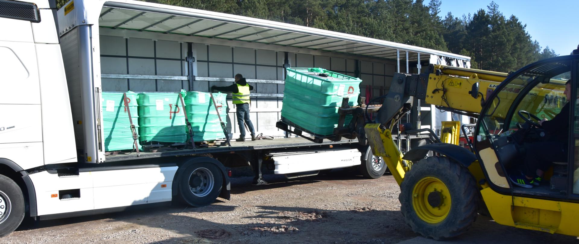 Na zdjęciu z prawej strony ładowarka teleskopowa, za pomocą której na naczepie samochodu ciężarowego jest umieszczany kolejny mauzer.
