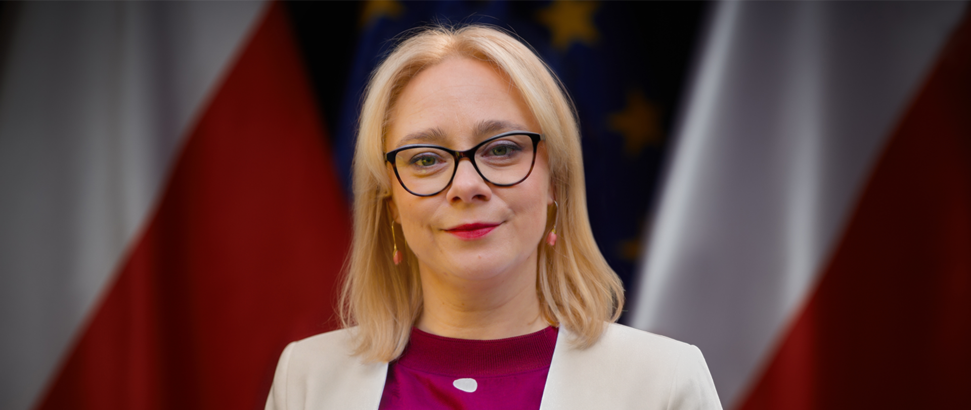 Wiceminister sportu i turystyki Żaneta Cwalina-Śliwowska na tle flag Polski i UE.