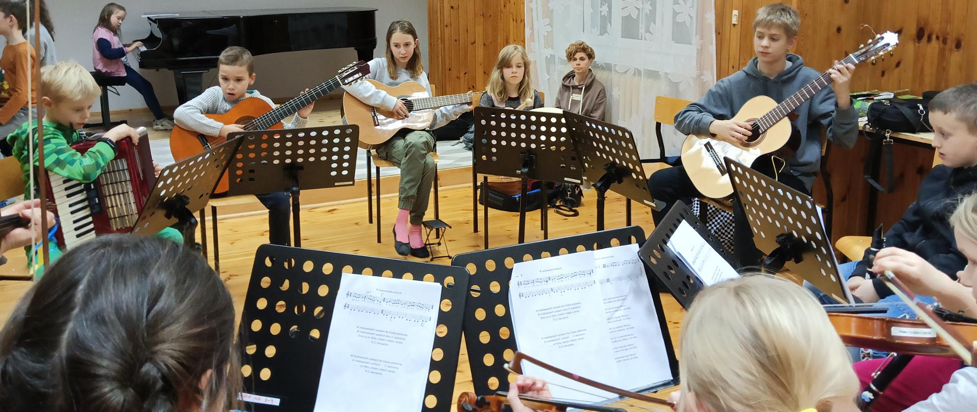 Zdjęcie przedstawia dzieci grające na instrumentach w sali kameralnej szkoły