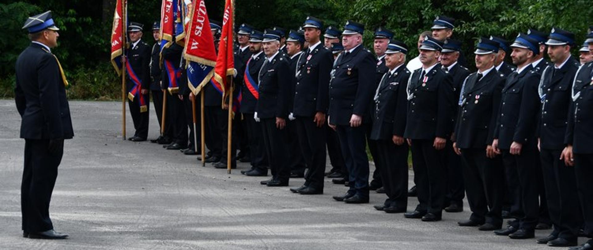 Dowódca uroczystości stojący na przeciwko pocztów sztandarowych i strażaków.