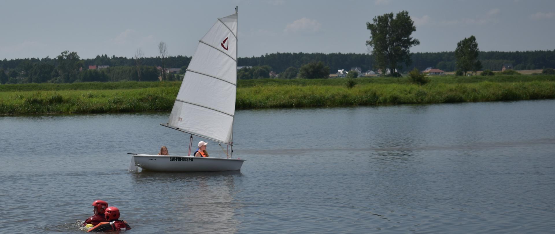 Zdjęcie przedstawia podejmowanie poszkodowanego z akwenu wodnego przez zabezpieczonego strażaka. 