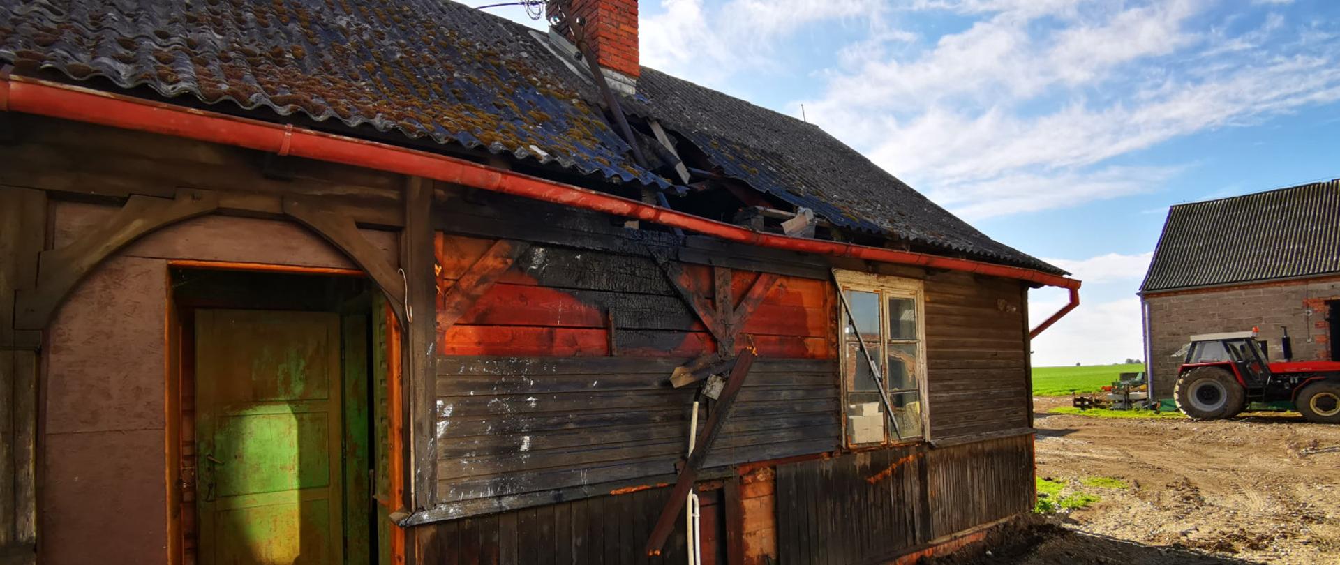 Widać budynek gospodarczy, drewniany, dach z eternitu, nadpalona przednia ściana