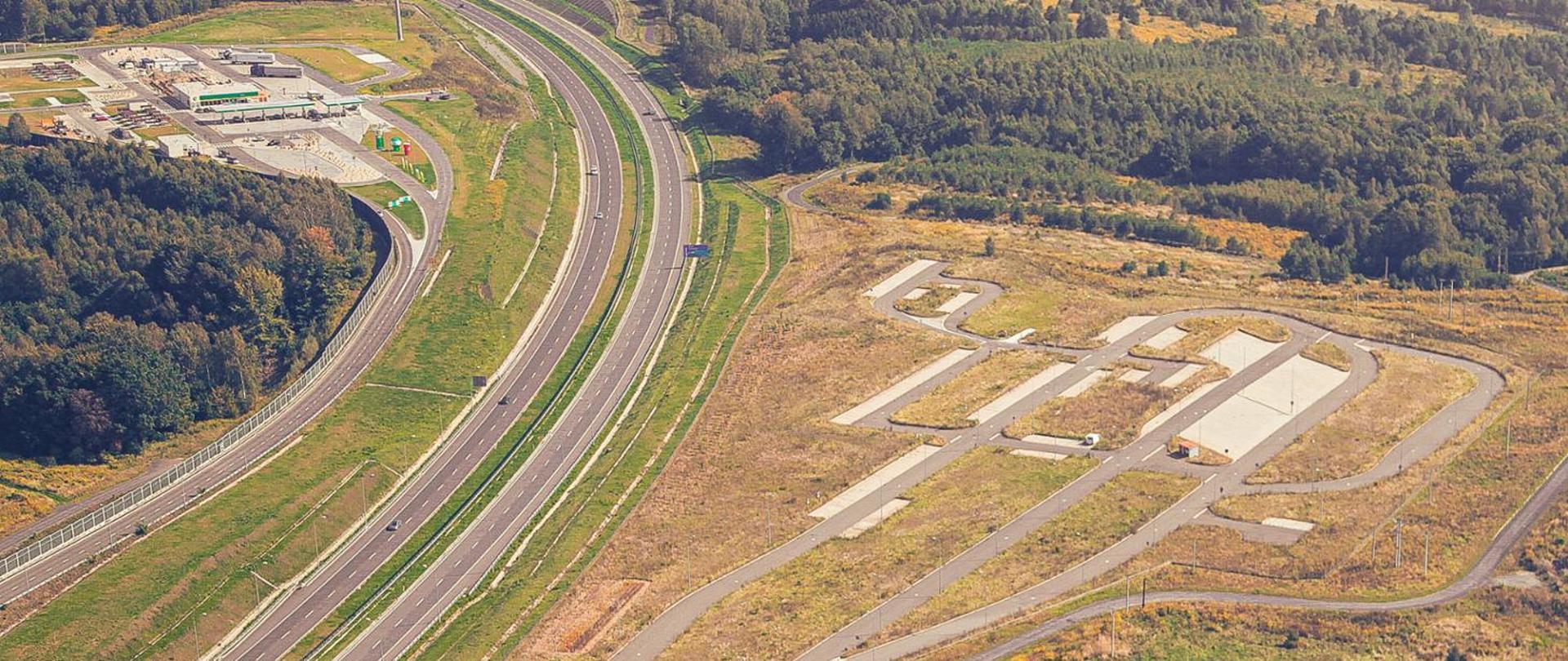 Fotografia lotnicza autostrady A1 w rejonie lokalizacji Miejsc Obsługi Podróżnych Mszana. W prawej części fotografii widoczna infrastruktura drogowa — miejsca parkingowe oraz jezdnie manewrowe MOP Mszana Południe. Po prawej MOP Mszana Północ wraz z infrastrukturą przewidzianą w kategorii II w postaci stacji paliw oraz obiektów usługowo-handlowo-wypoczynkowych