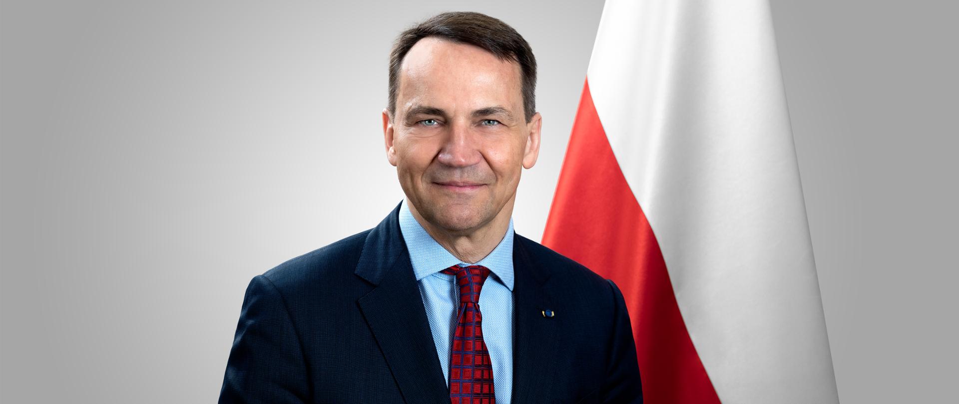 Minister Spraw Zagranicznych Radosław Sikorski na tle flagi Polski