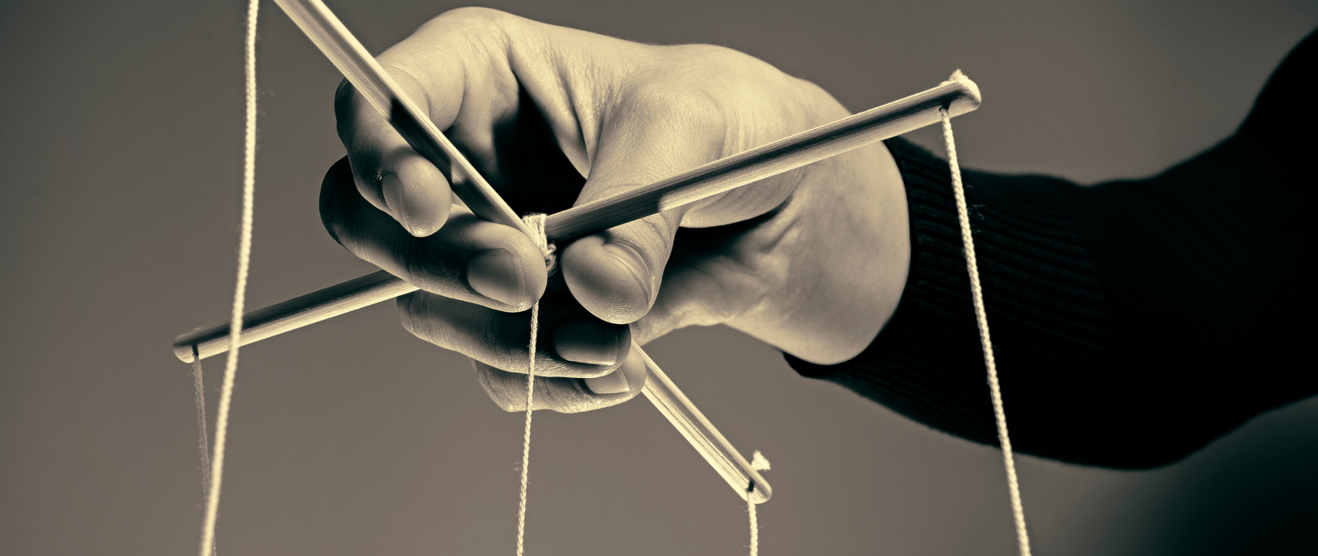 Dłoń trzymająca krzyżak z przymocowanymi sznurkami do poruszania lalką-marionetką