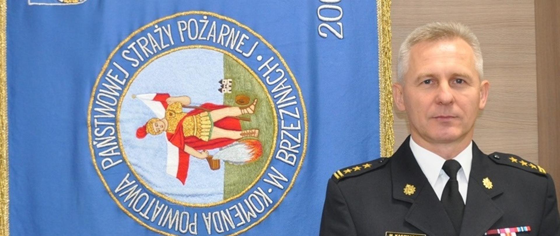 Zdjęcie profilowe zastępcy Komendanta Powiatowego na tle sztandaru Komendy Powiatowej PSP w Brzezinach