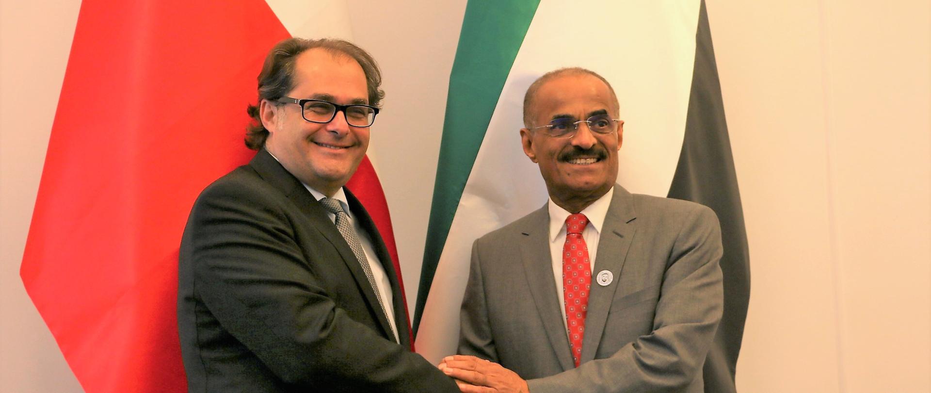 Wspólne zdjęcie - uścisk dłoni obu ministrów na tle flag Polski i ZEA