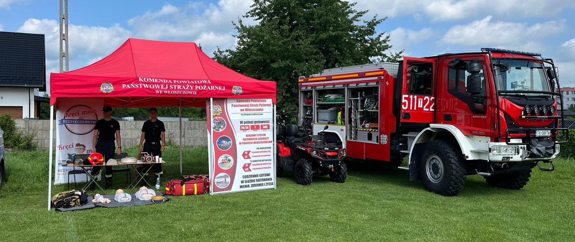 Na zdjęciu znajduję się wóz strażacki, quad oraz namiot. W namiocie stoją strażacy, którzy przygotowują wystawę sprzętu oraz stanowisko do nauki pierwszej pomocy.